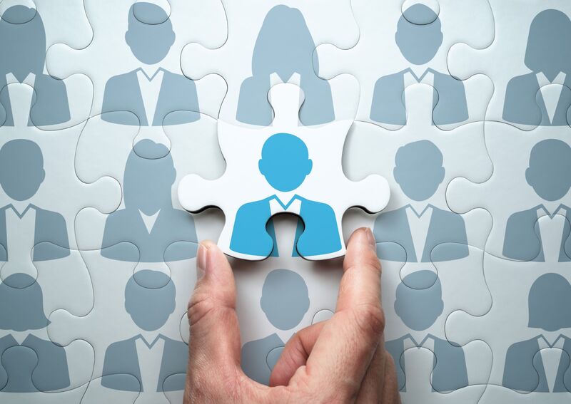 Photo; a hand places the last piece of a puzzle; puzzle pieces with graphics of business people